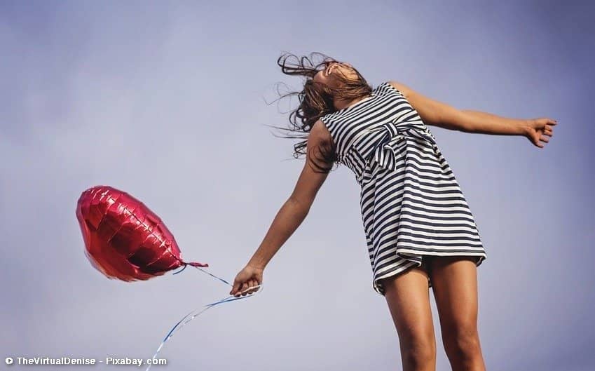 Frau macht Luftsprung, hält Luftballon in der Hand